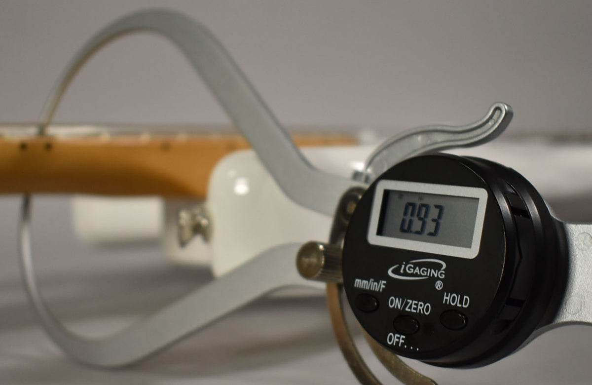 A digital caliper measures the guitar's neck thickness at 0.93 inches, with the maple fretboard visible in the background.