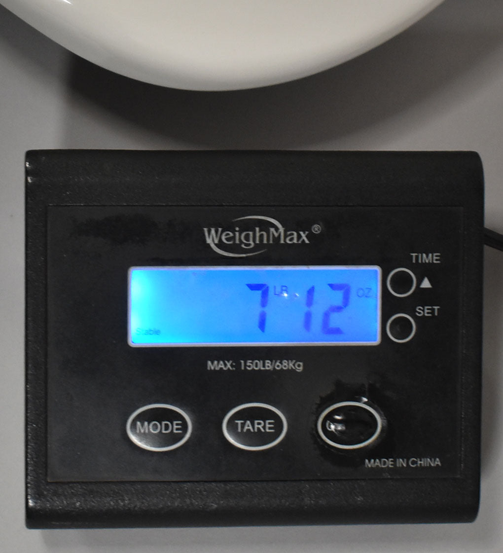A black digital scale displays "7 LB 12 OZ" in bright blue, with a white guitar body curving above.