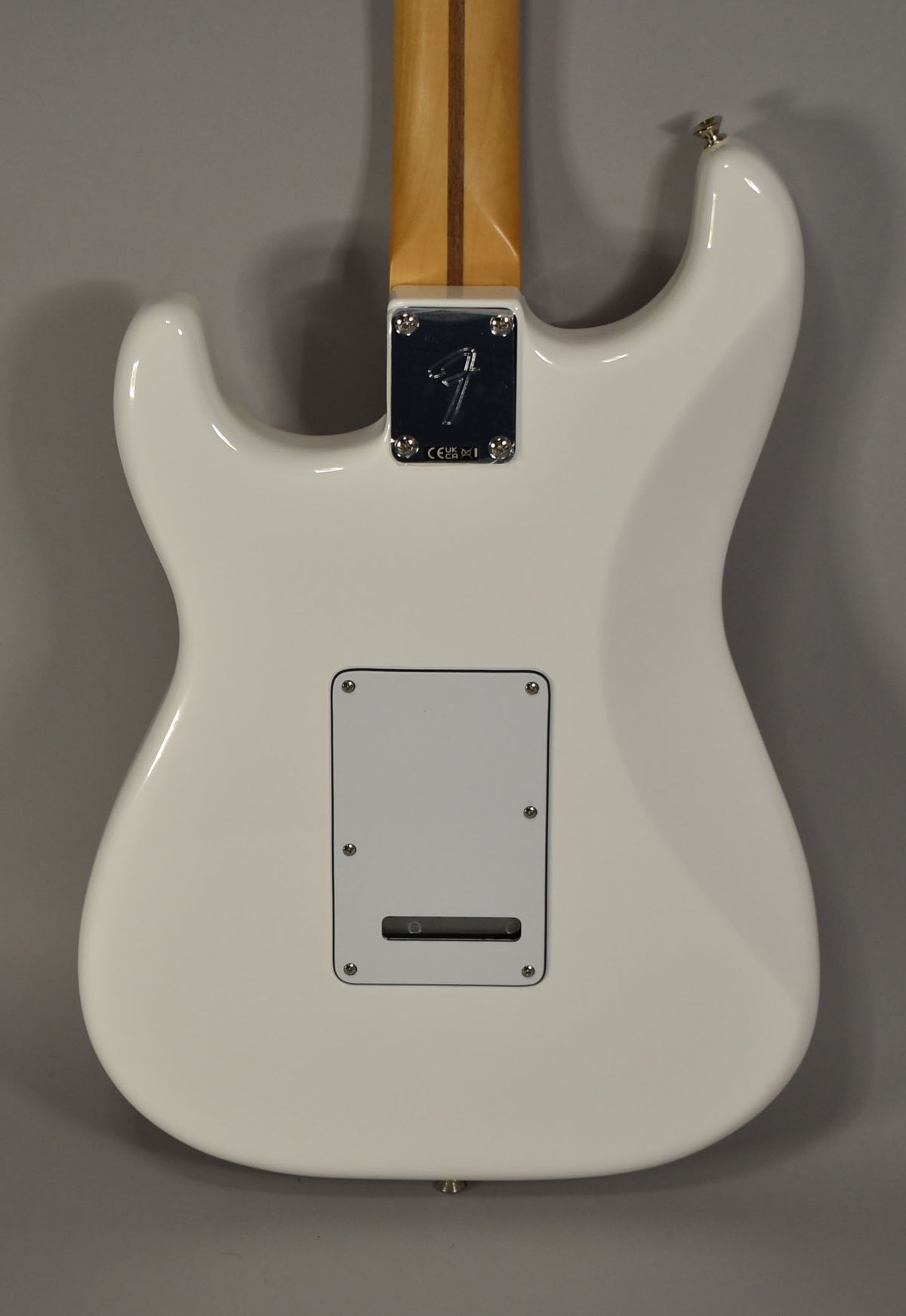 The back of a glossy white Stratocaster body, showing the neck plate, a light maple neck, and a rectangular tremolo cover.