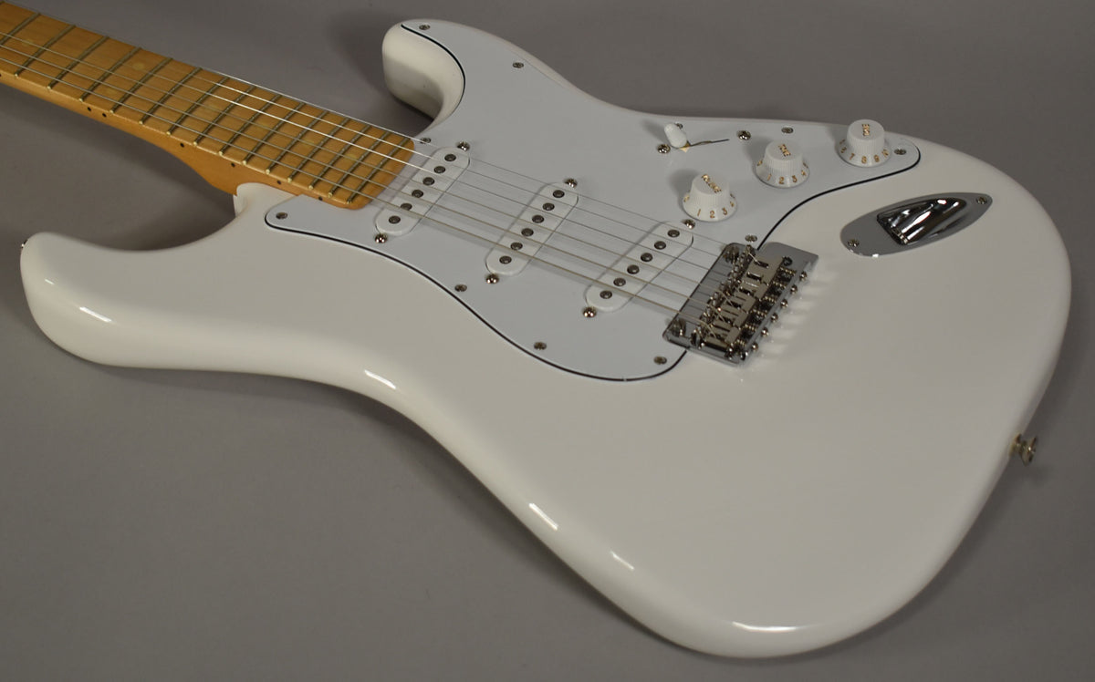 A polar white Stratocaster, angled from the upper left, showing the maple neck, white pickguard, three single-coil pickups, and chrome hardware.