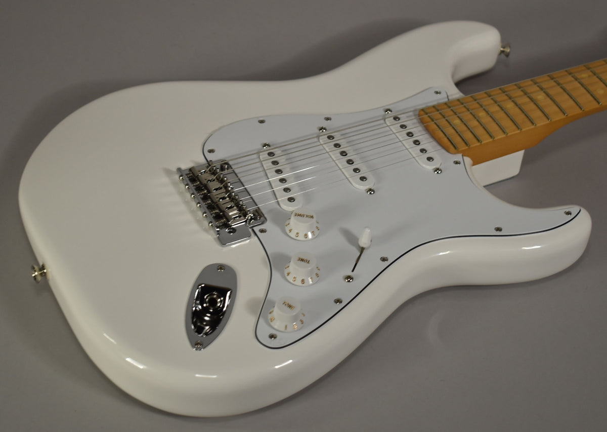 The white Stratocaster body, pickguard, and three single-coil pickups are visible from above, with a maple neck and chrome hardware.