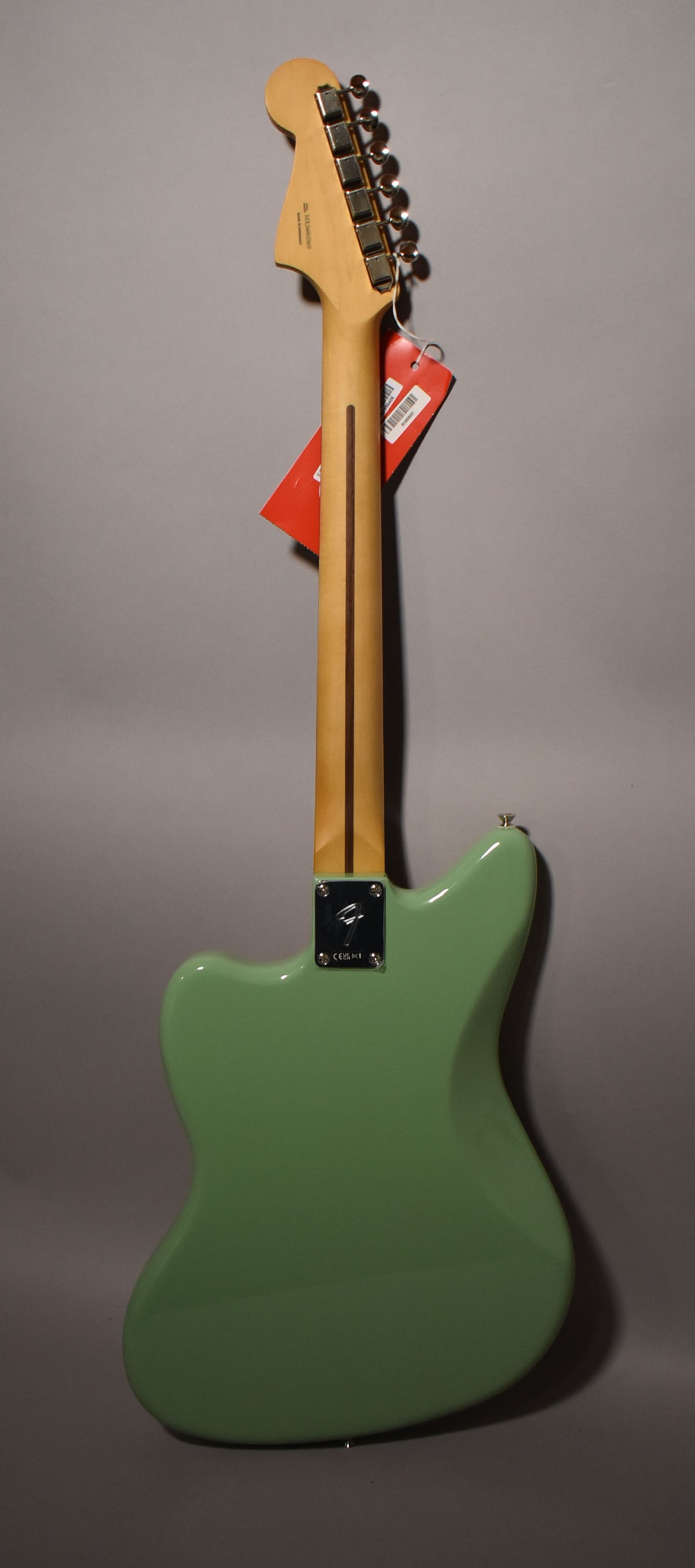The back of a glossy birch green Jazzmaster, with a light wood neck, chrome tuners, and a metal neck plate.