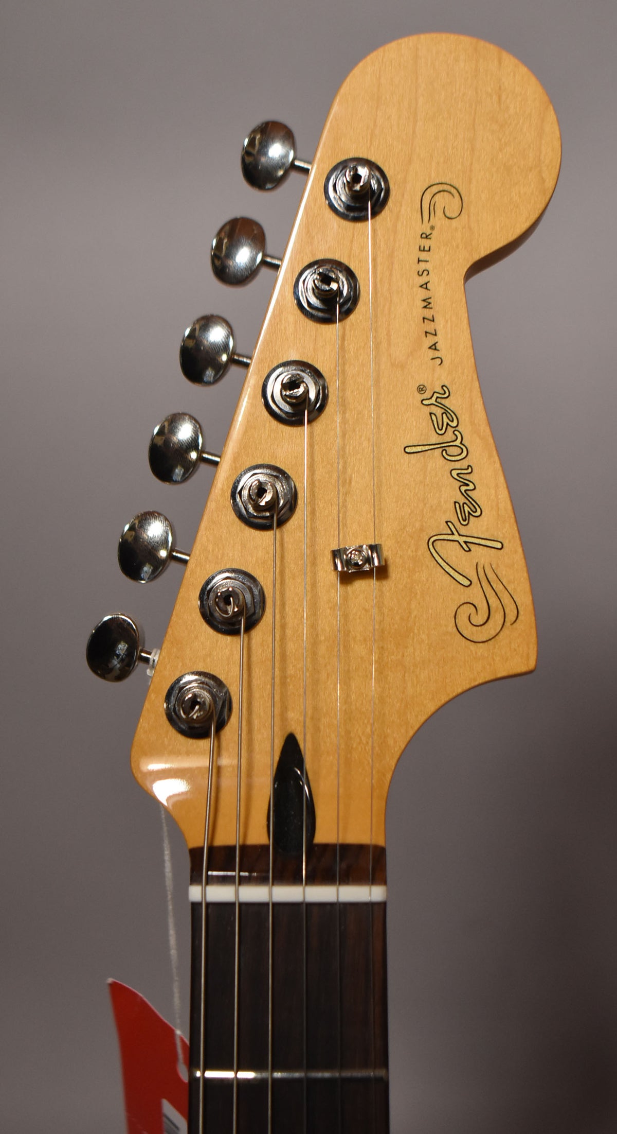 Close-up of the Jazzmaster's maple headstock and dark fretboard, showing six chrome tuners, a string tree, and a white nut.