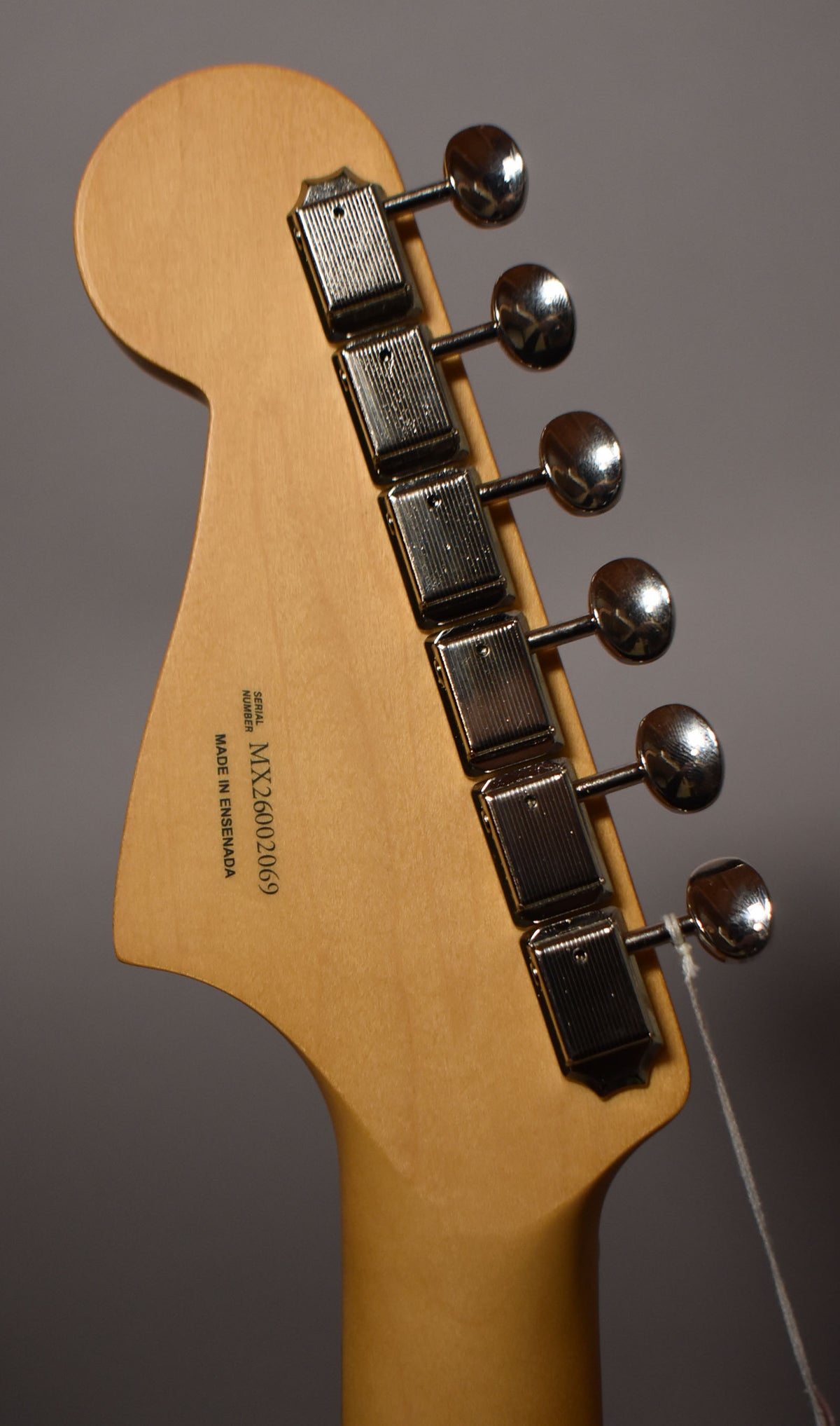 Rear view of the guitar's light wood headstock and neck, showing six chrome tuners with ribbed casings and a serial number.