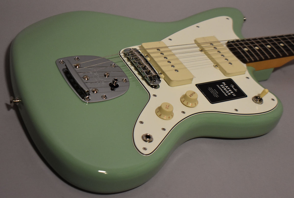 The glossy birch green Jazzmaster body is angled from the upper left, showing its white pickguard, cream pickups, and chrome tremolo.