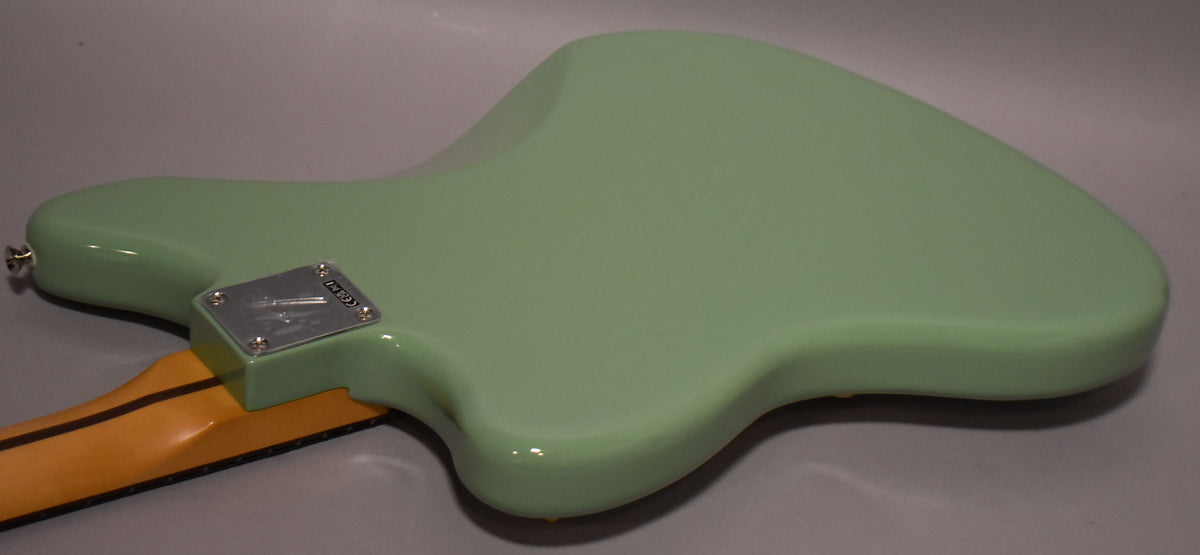The back of a glossy birch green Jazzmaster body is angled from the neck joint, showing the chrome neck plate and strap button.
