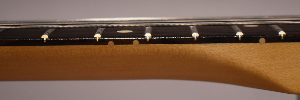Close-up of the guitar's fretboard, showing dark wood, light fret markers, and the natural wood neck from the side.
