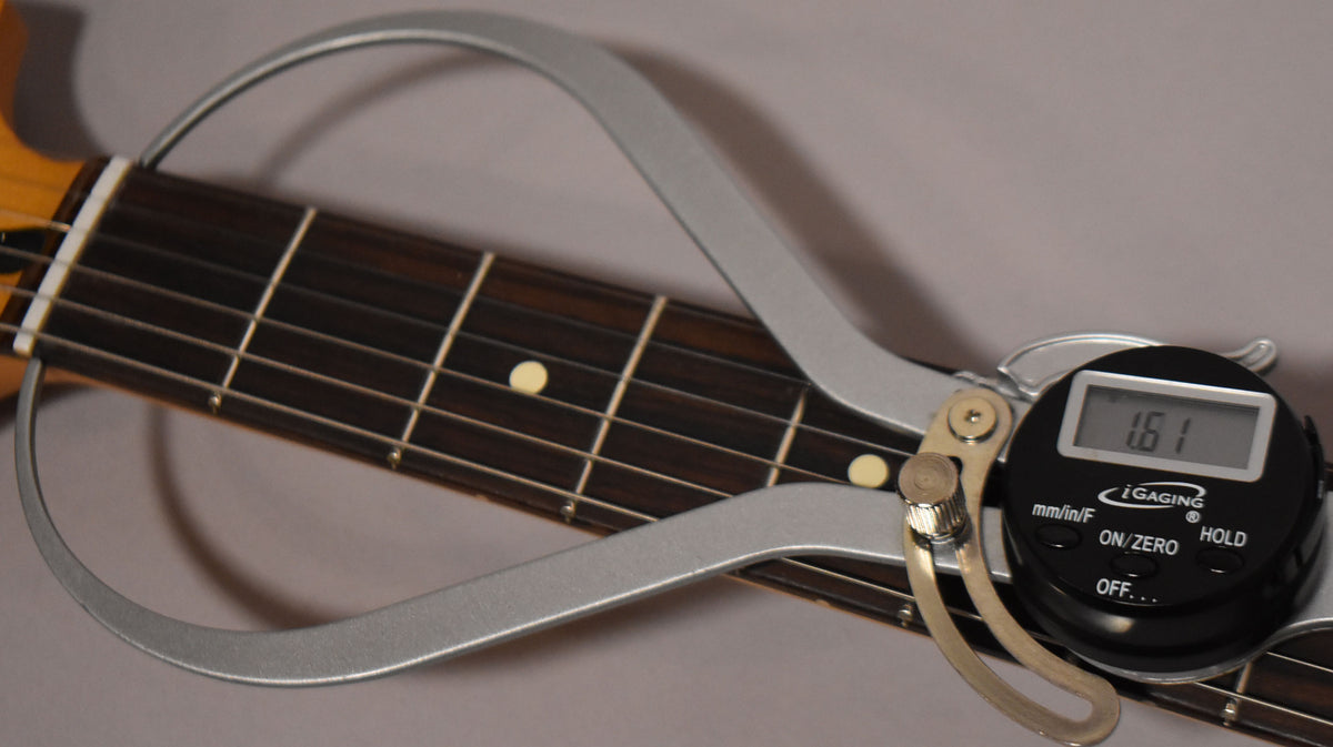 Close-up of the guitar's dark fretboard with cream dot inlays, showing a digital caliper measuring the string height at 1.61mm.