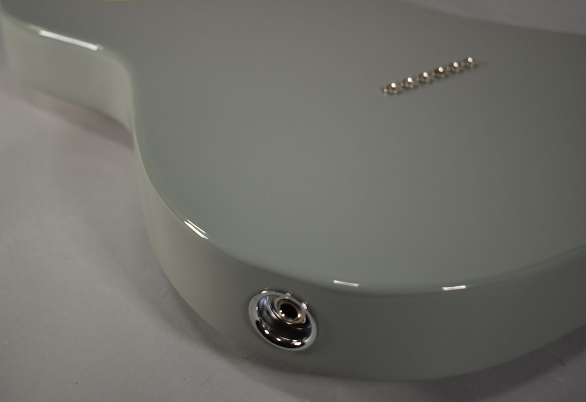 The lower bout of a glossy Cactus Gray Telecaster body, showing the chrome output jack and six string-through-body ferrules.