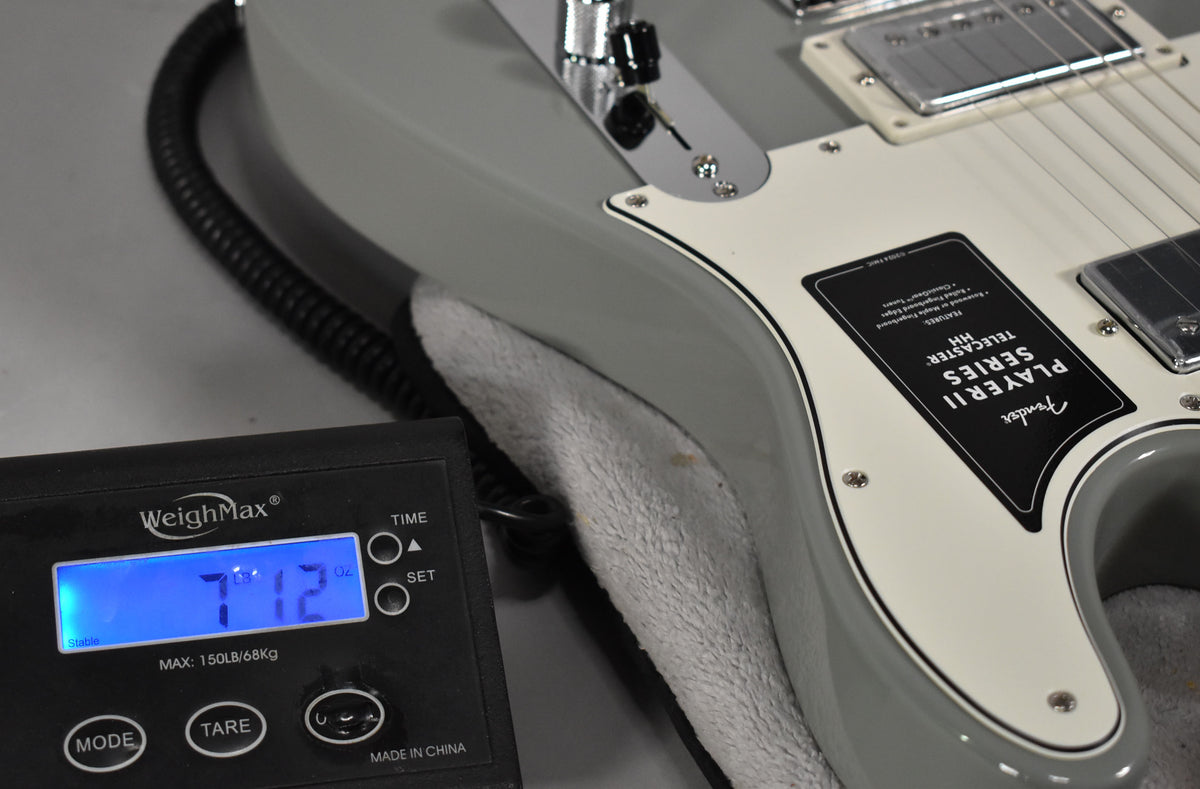 The Cactus Gray Telecaster's body and pickguard are shown from above, with a scale displaying 7lb 1.2oz in the foreground.