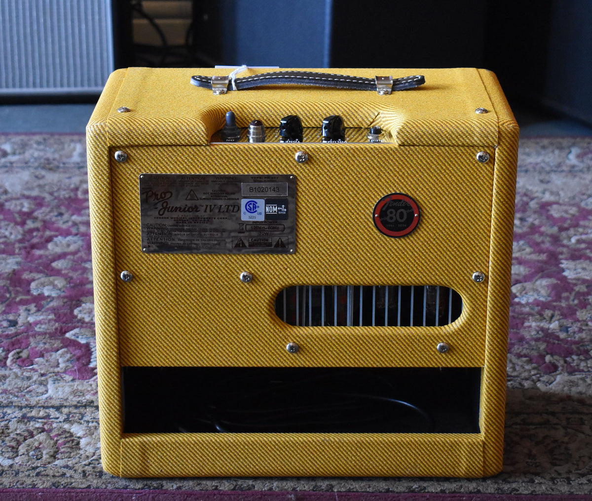 Front view of a tweed combo amp with a dark brown leather handle, black control knobs, and a metal serial plate.