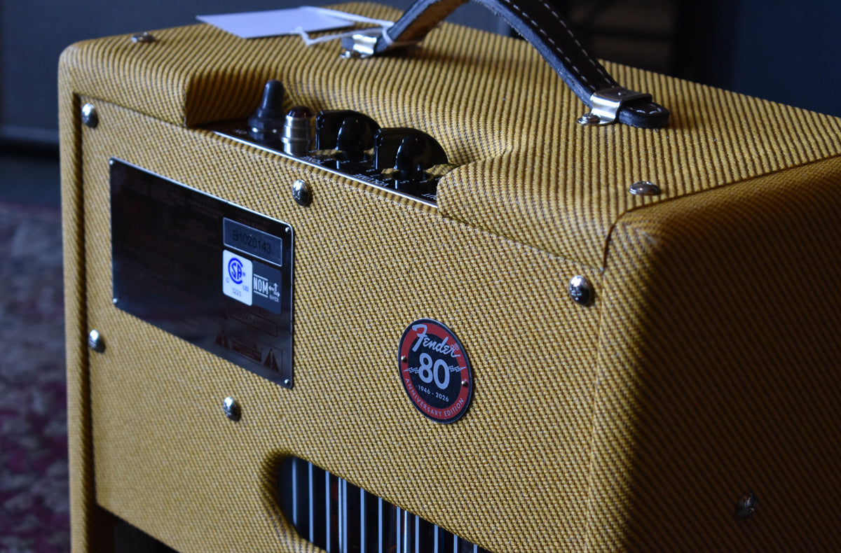 Close-up of the tweed amp's top and right side, showing the black control knobs, leather handle, and an 80th Anniversary badge.