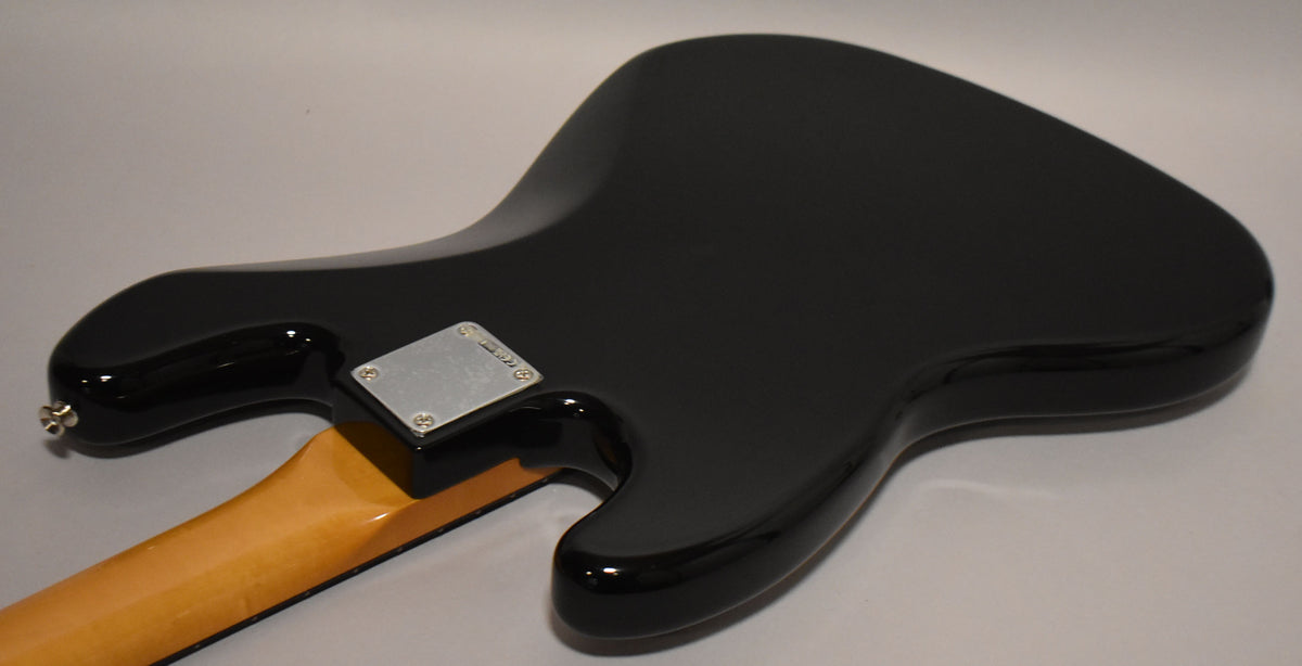 The back of a black Jazz Bass body, showing the neck plate and the light-colored neck heel, with a strap button visible.