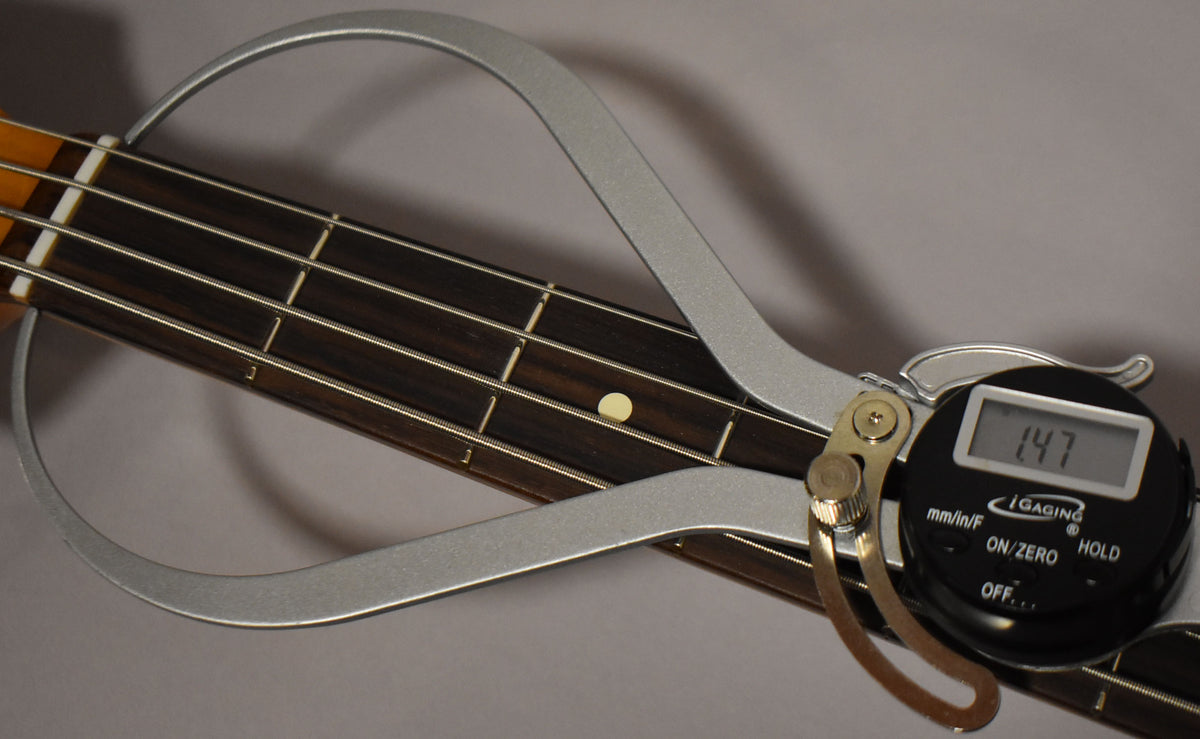 Close-up of the bass's dark fretboard with a digital fret rocker measuring the 7th fret, displaying "1.47".