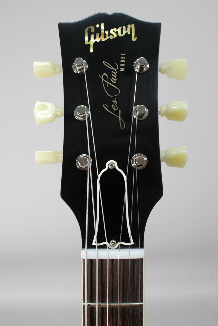 Close-up of the black headstock with gold lettering, six cream tuning pegs, and a white bell-shaped truss rod cover.