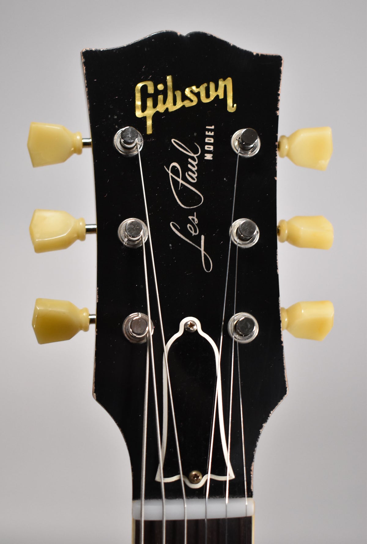 Close-up of the ebony headstock with light aging, showing six cream tuning pegs, string trees, and a bell-shaped truss rod cover.