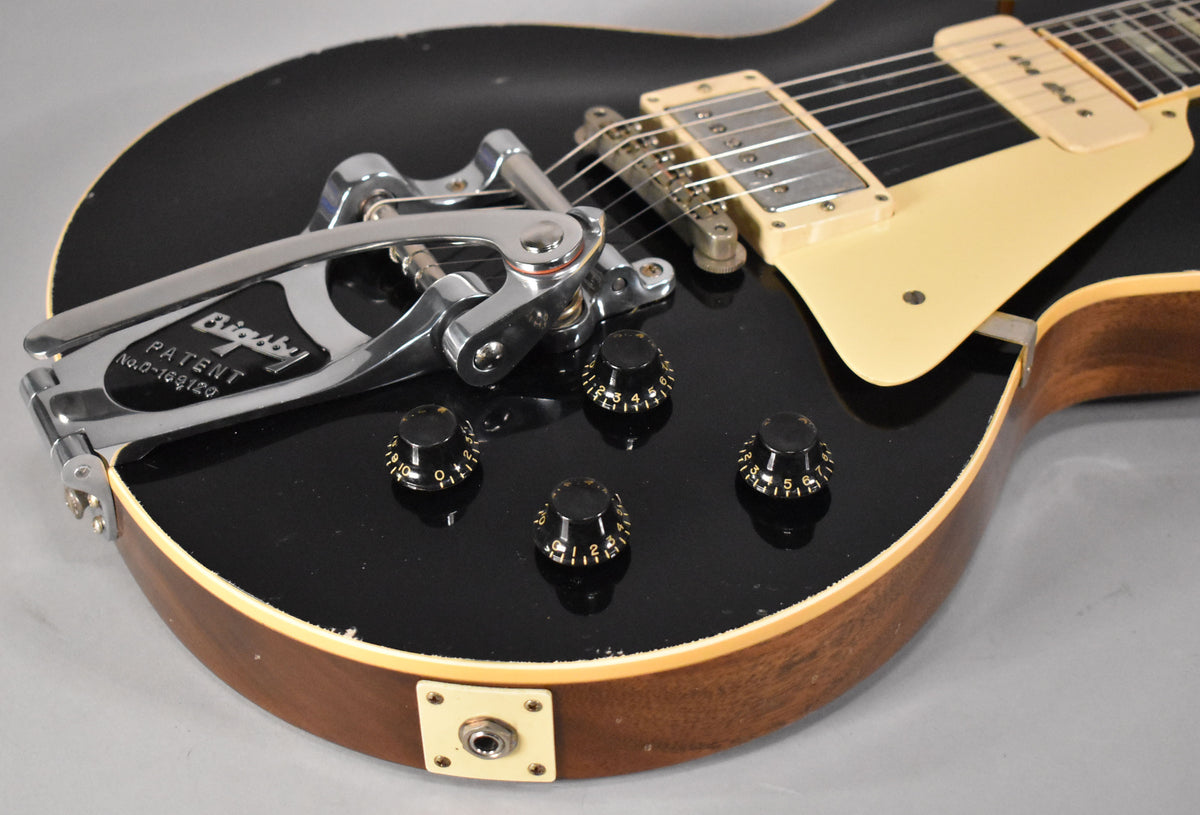 Close-up of the ebony Les Paul's lower body, showing the Bigsby tremolo, four black control knobs, cream pickguard, and output jack.