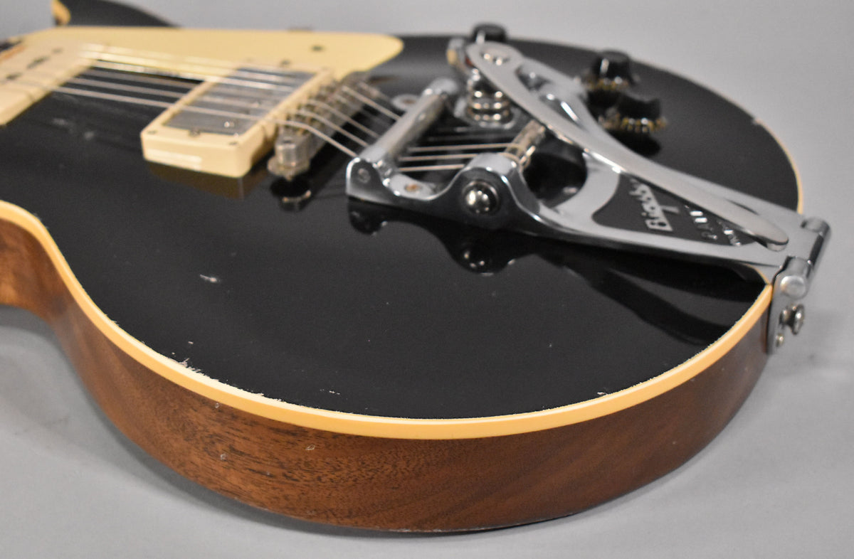 Close-up of the guitar's lower body, showing the ebony finish with light aging, cream binding, Bigsby tremolo, and bridge pickup.