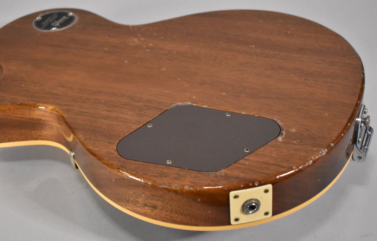 The guitar's mahogany back and side are visible, showing a control cavity cover, output jack, and light aging with finish checking.