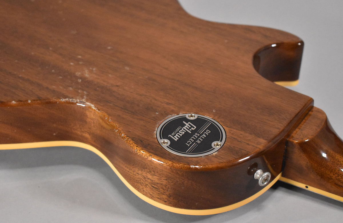 The guitar's dark brown back and neck heel are shown, with a black "Dealer Select" medallion and visible finish checking.