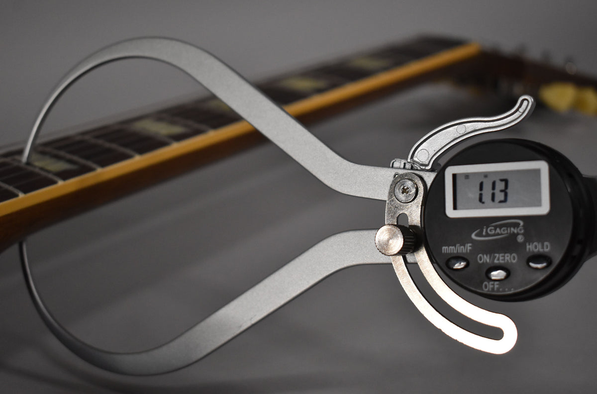 A digital caliper measures the fret height on the guitar's neck, showing "1.13" on its screen.