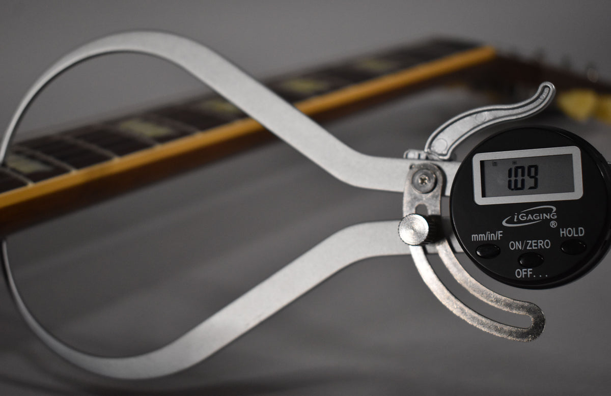A digital caliper measures the guitar's neck, showing "1.09" on its screen, with the fretboard visible in the background.