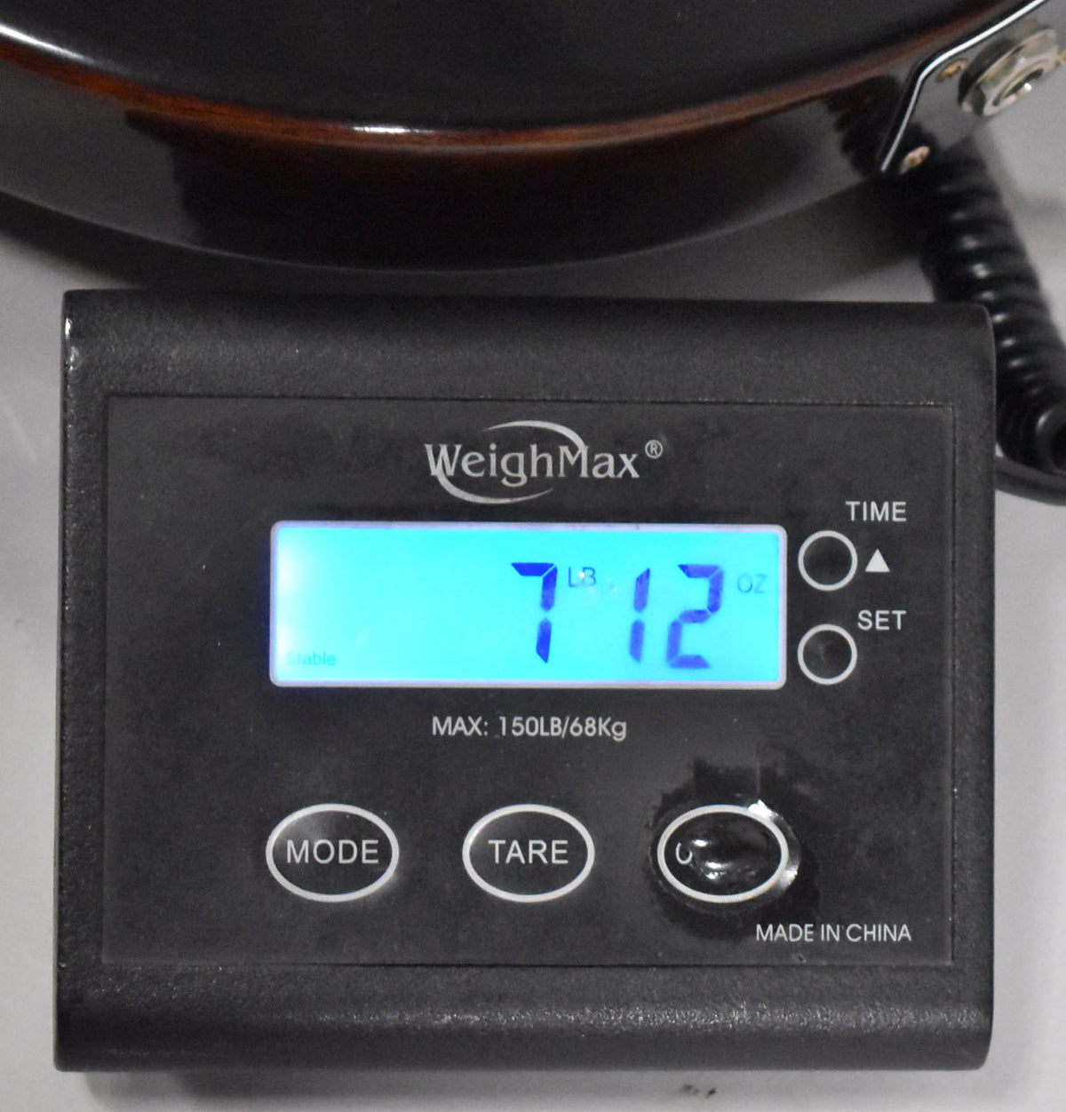 The guitar's dark brown body rests on a black digital scale displaying "7 LBS 12 OZ" in bright blue.