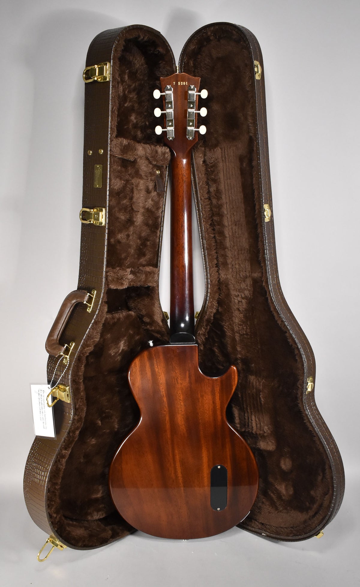 The guitar's back and headstock are visible, showing a rich, glossy mahogany finish and six white-button tuners.