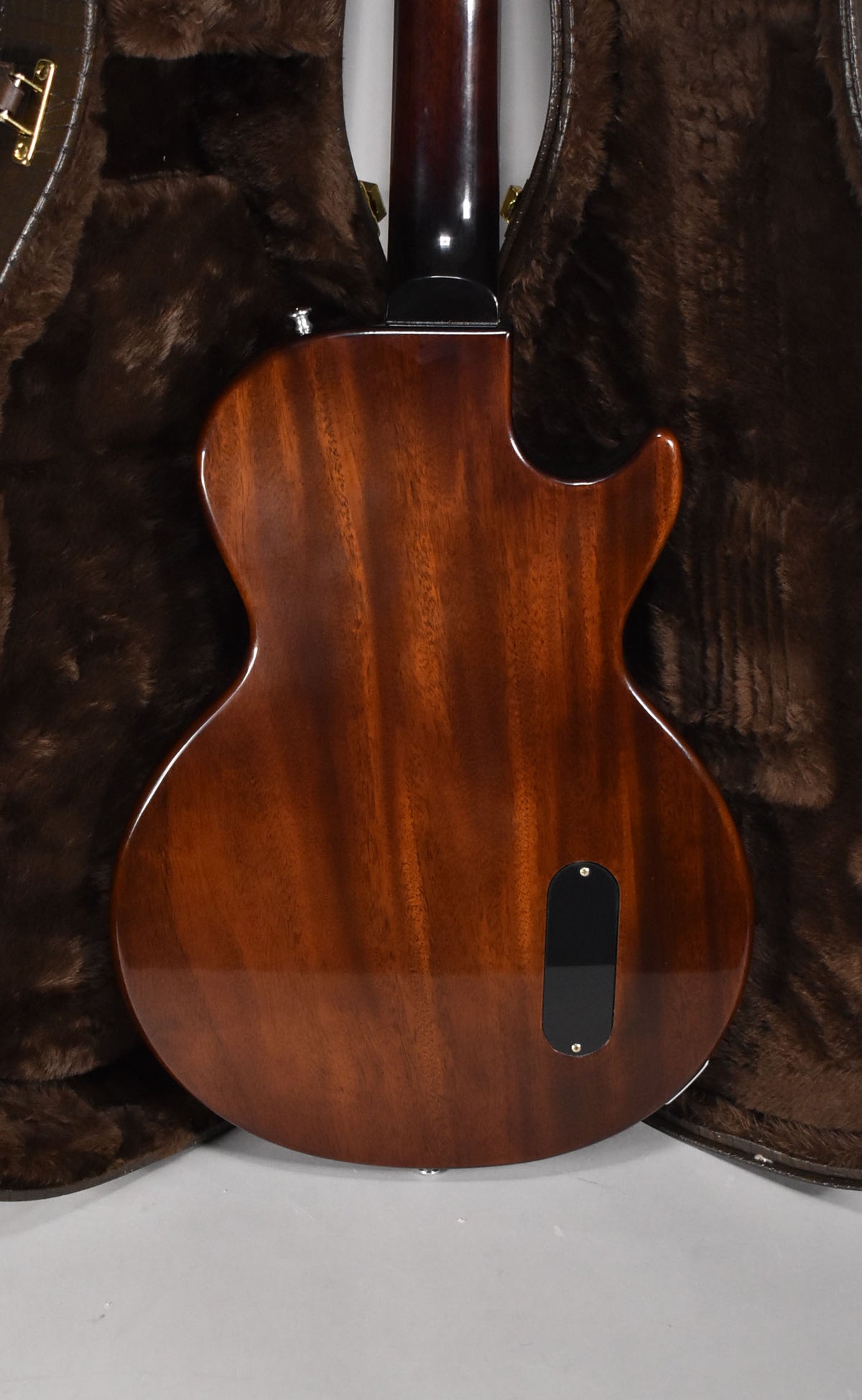 The back of a glossy, dark reddish-brown guitar with visible wood grain, a black control cavity cover, and a strap button.