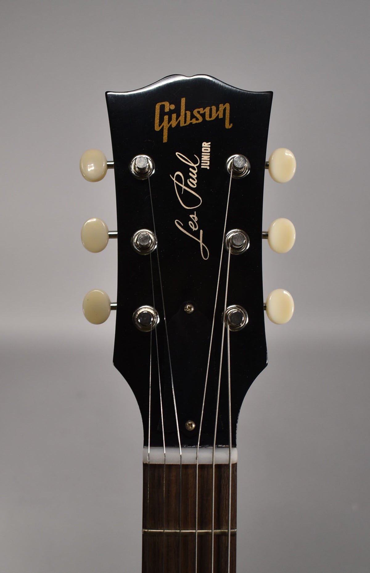 The black headstock, with six cream tuning pegs, is centered and angled slightly down towards the dark fretboard.