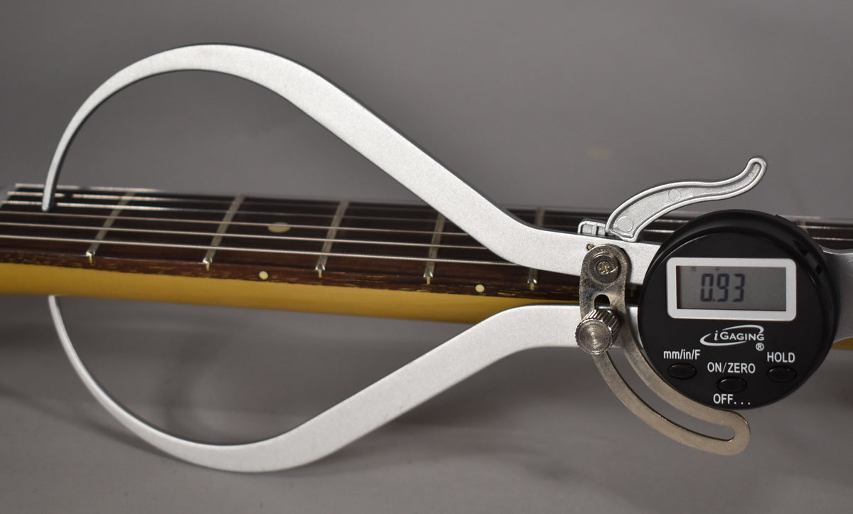 A digital caliper measures the guitar's fretboard and strings, showing a reading of 0.93.