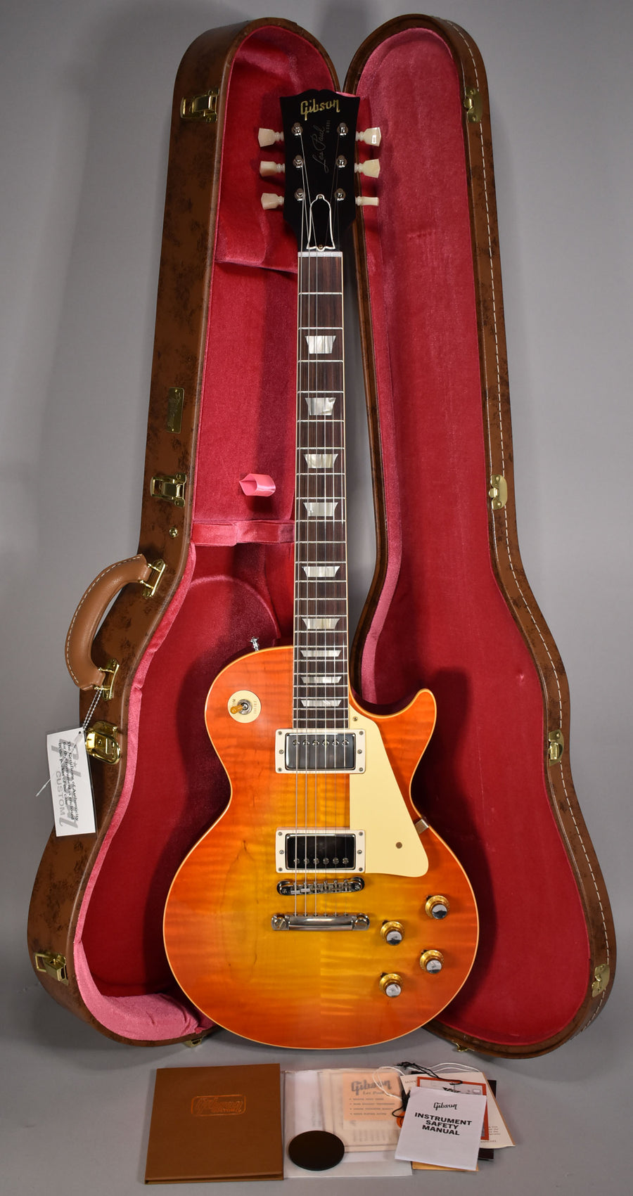 Full-length view of a sunburst Les Paul with a flamed maple top, cream binding, and nickel hardware, resting in its open brown case.