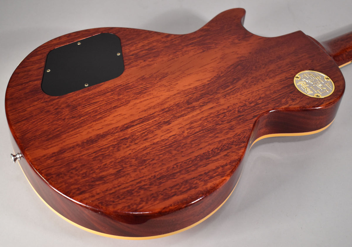 The guitar's back is a rich reddish-brown with visible wood grain, a black control cavity cover, and a gold medallion.