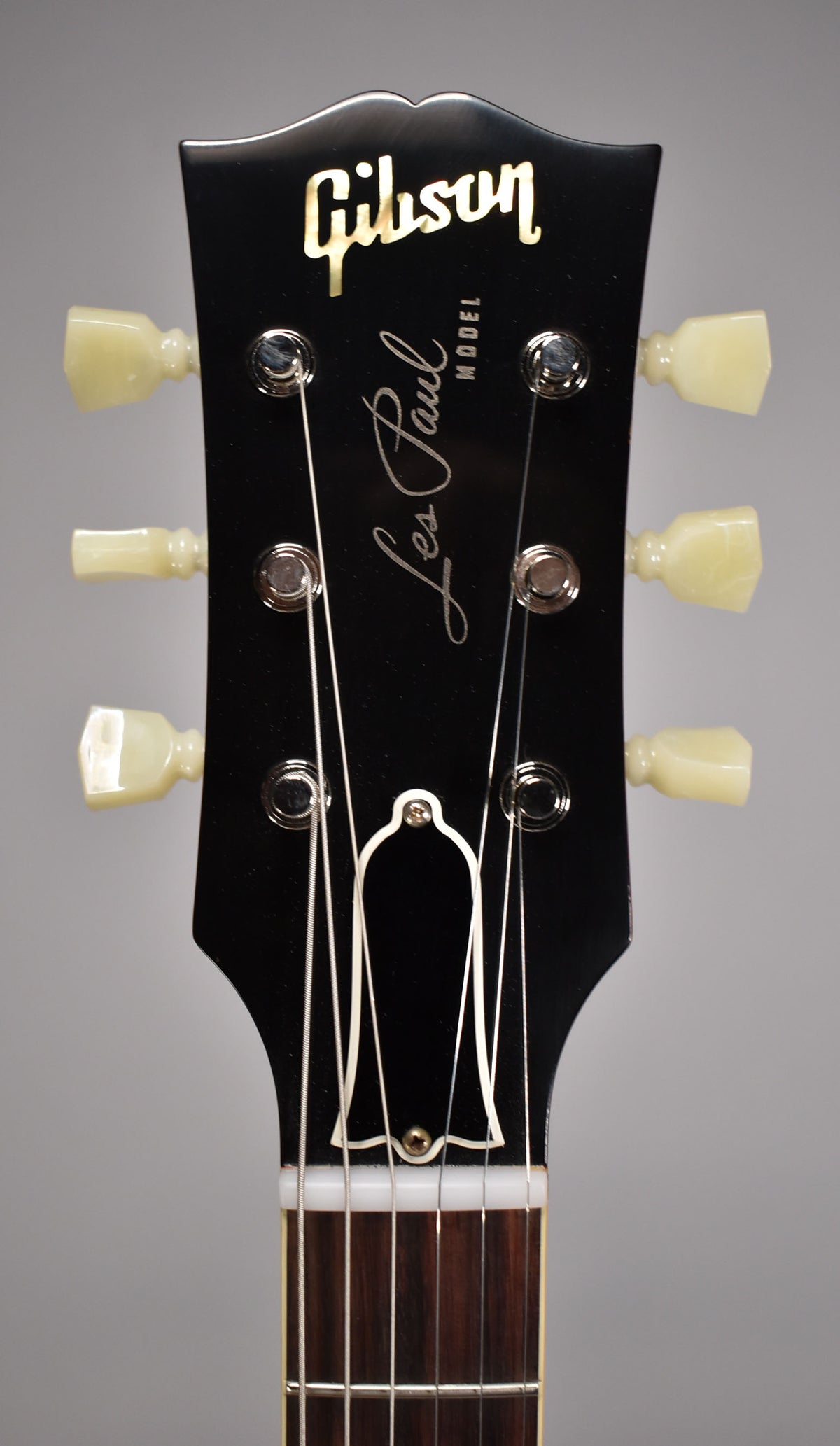 The black headstock, with a white truss rod cover and cream tuning pegs, is centered, showing the top of the dark fretboard.