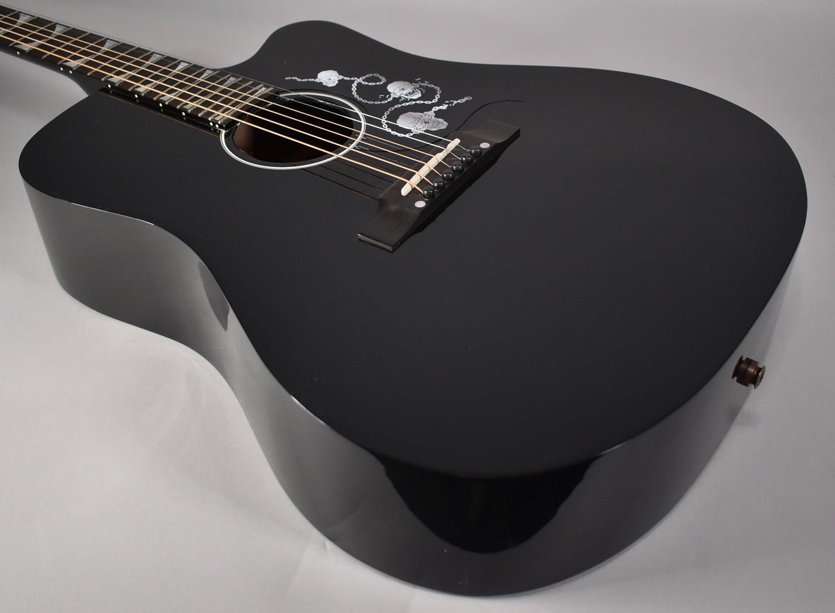 Angled view of the glossy black acoustic guitar's body, showing the soundhole, bridge, and intricate silver pickguard design.