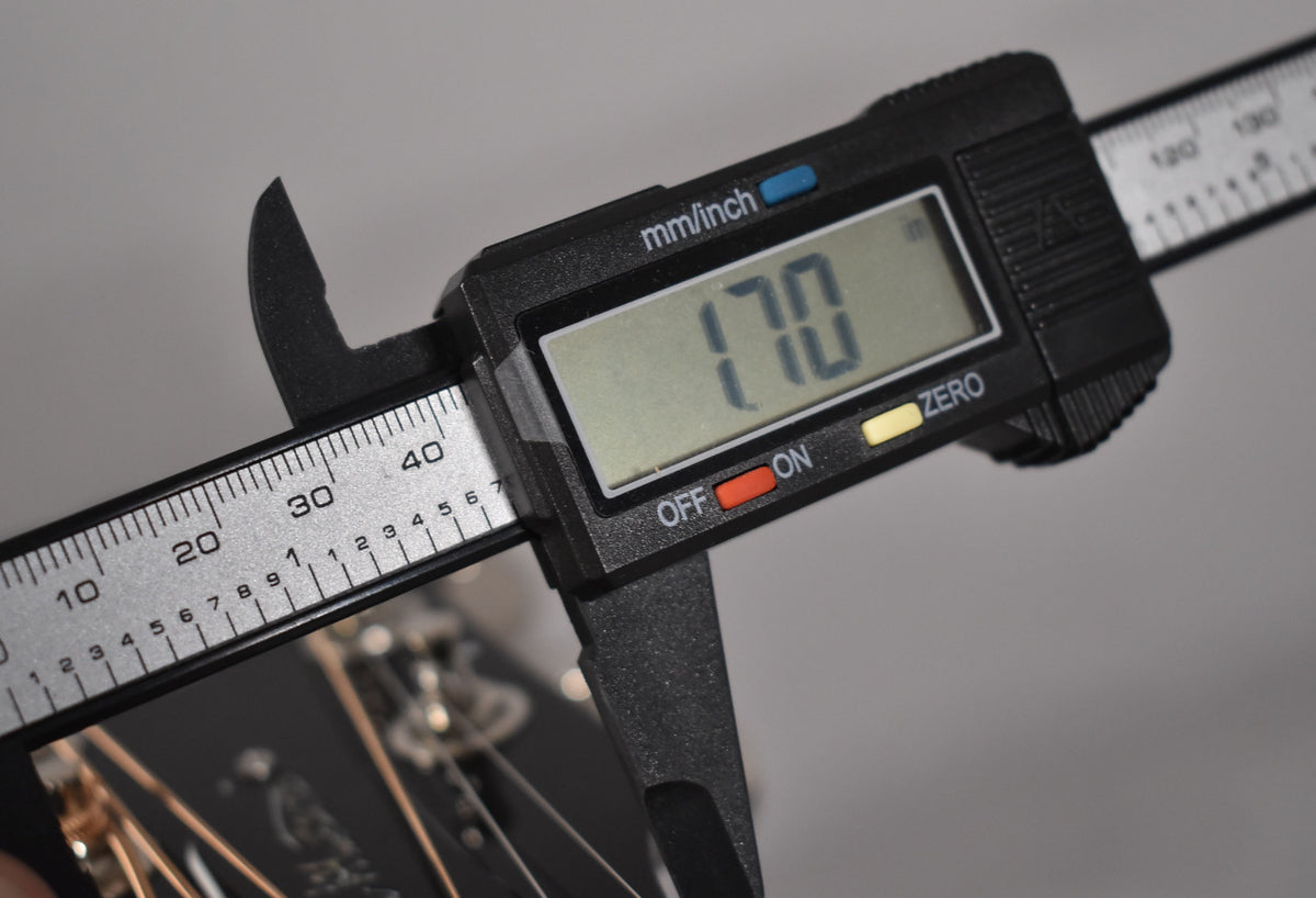 A digital caliper measures the guitar's nut width at 1.70 inches, with the headstock and strings visible below.