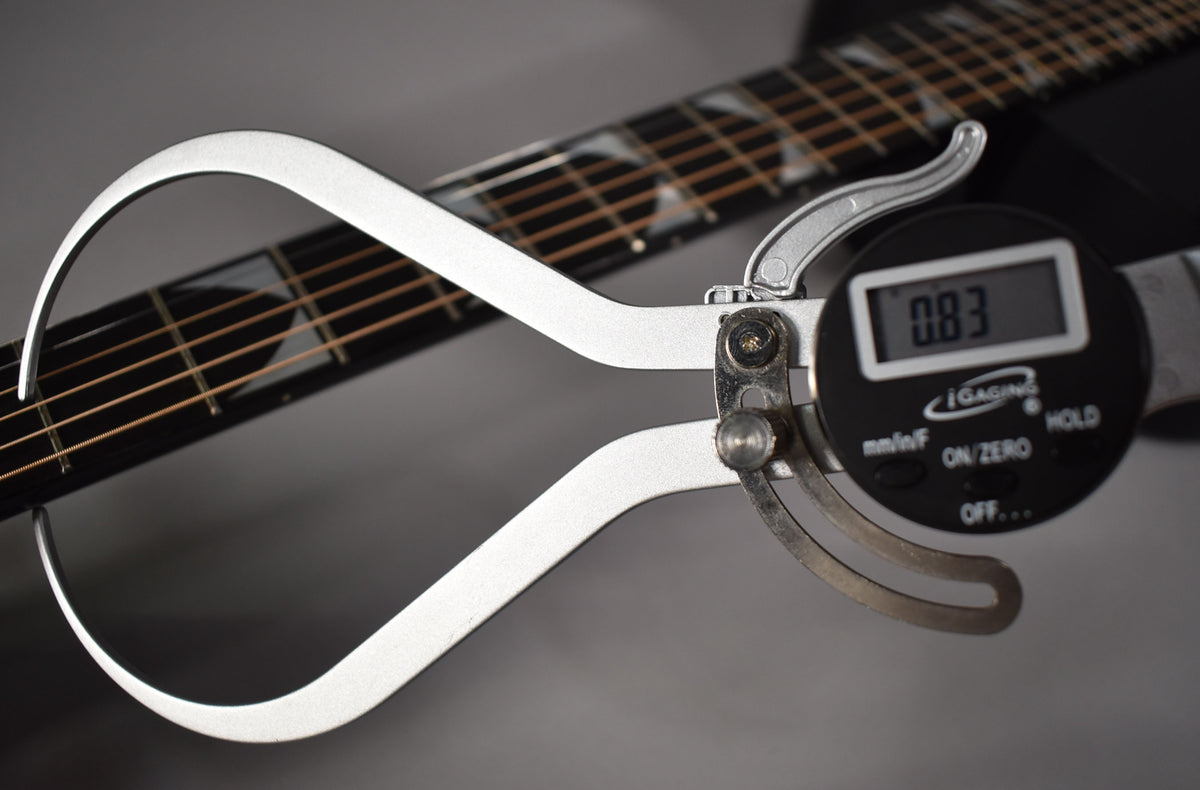 A digital caliper measures the guitar's ebony fretboard, showing a 0.83mm reading, with block inlays visible.