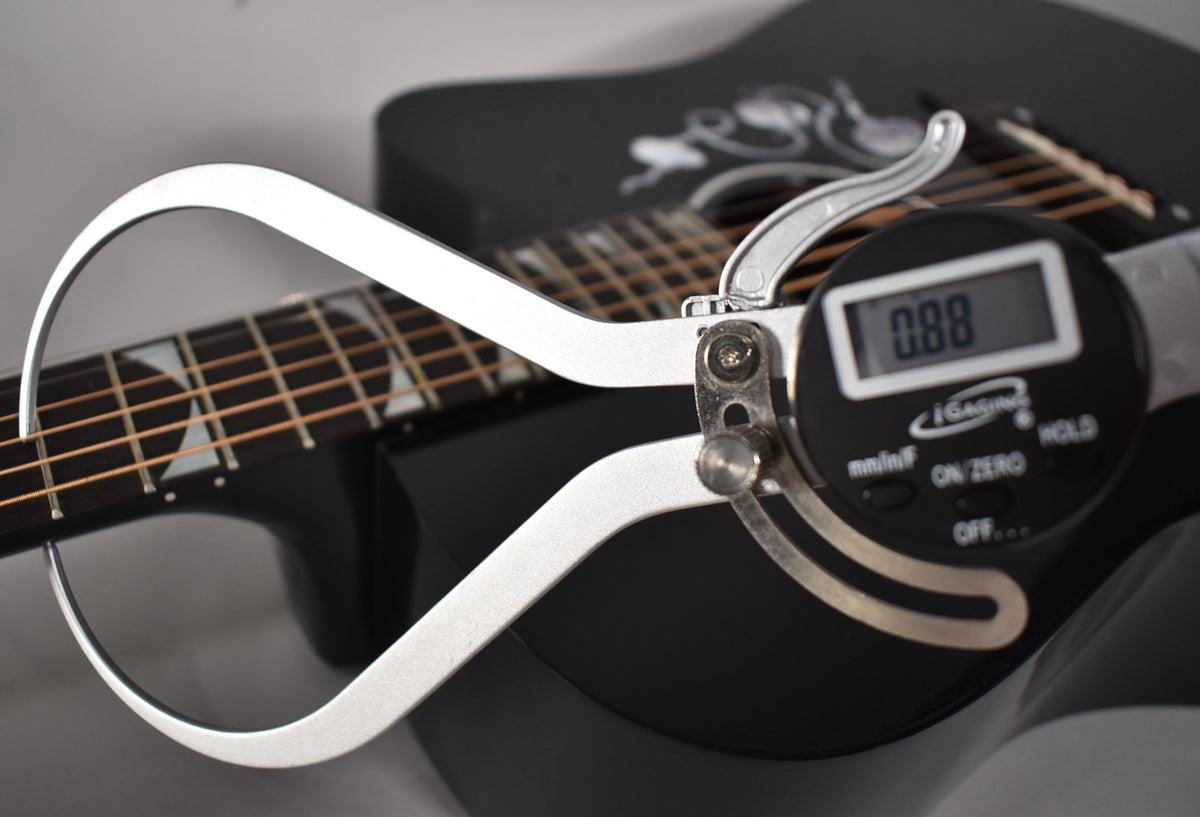 A digital caliper measures the string height above the fretboard on the guitar's glossy black body, showing 0.88mm.