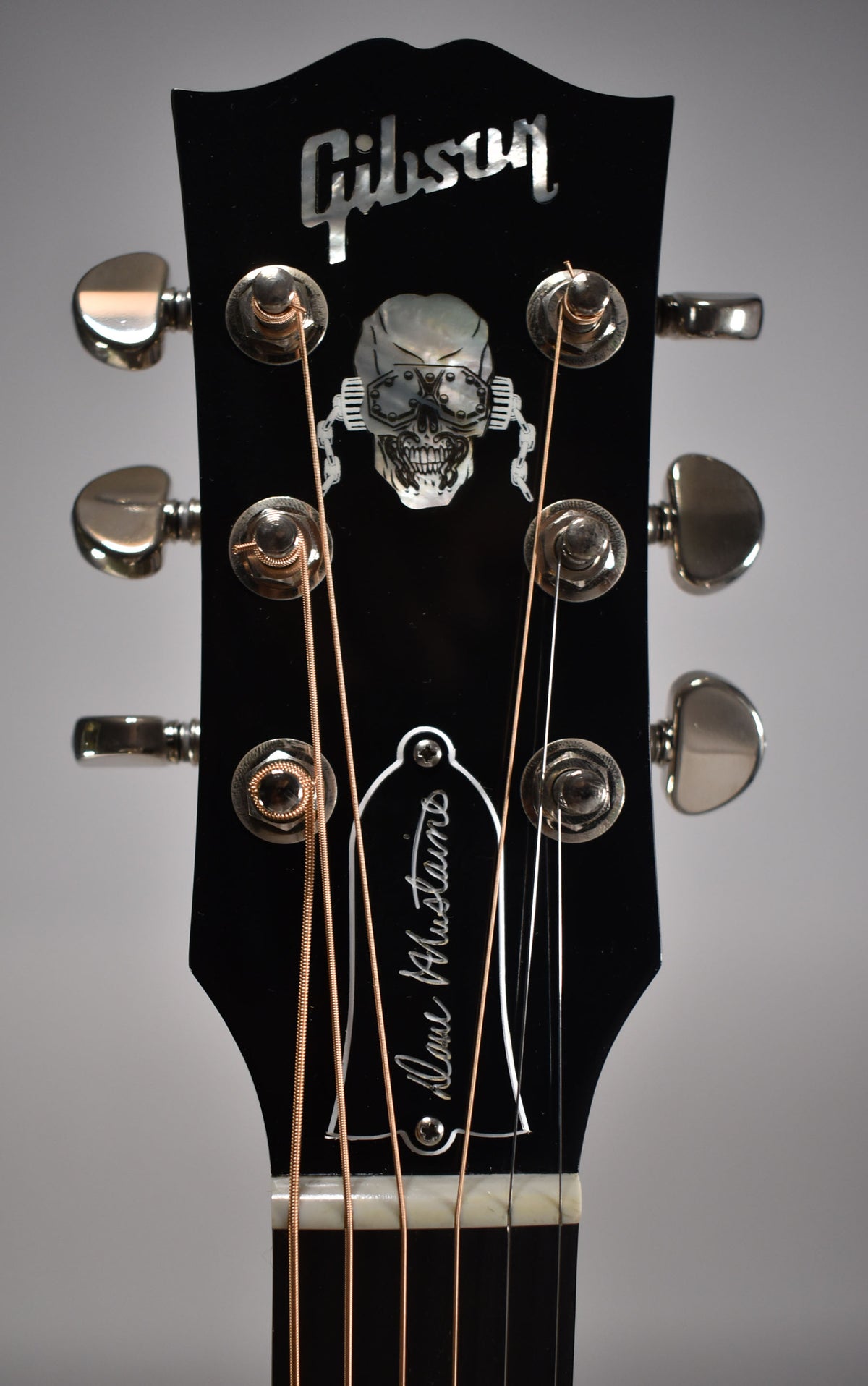 Close-up of the ebony headstock with a mother-of-pearl skull inlay, six chrome tuners, and a white truss rod cover.
