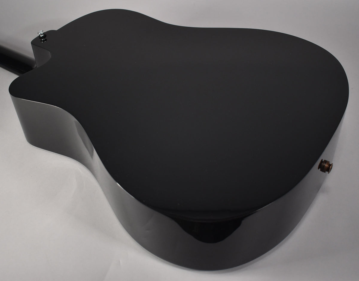 The glossy black acoustic guitar's back and side are angled, revealing a strap button on the lower bout and another on the neck heel.