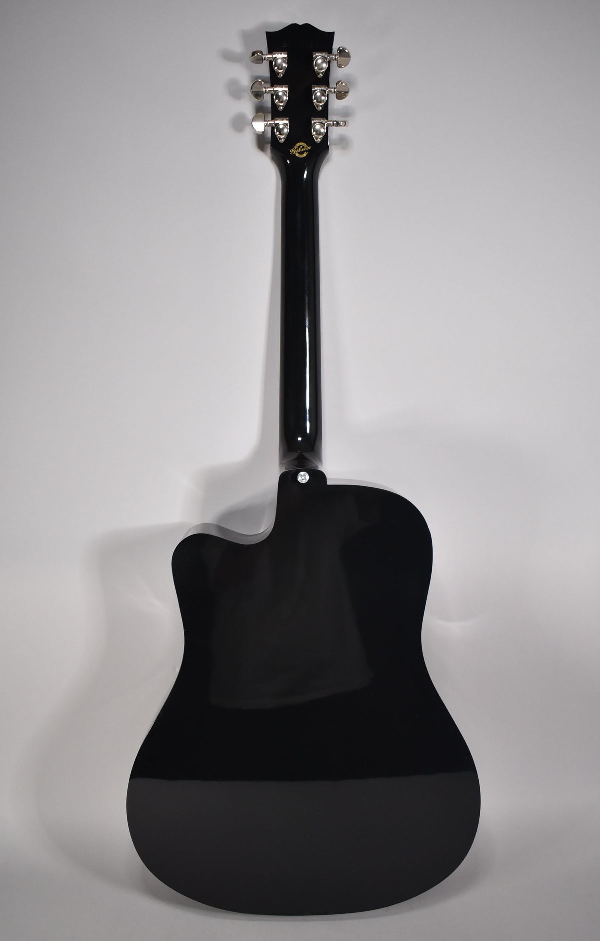 The back of a glossy black acoustic guitar with a cutaway, showing the headstock with six chrome tuners.