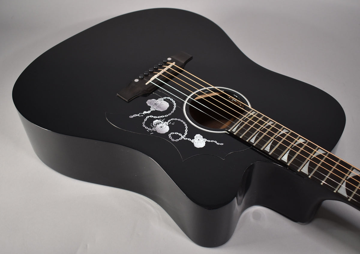 The ebony acoustic guitar's body and cutaway are angled from above, revealing skull and chain inlays on the pickguard.