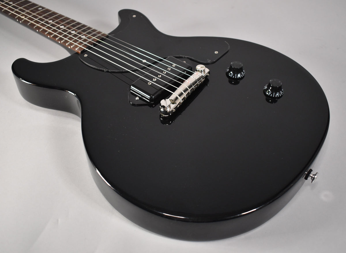 Glossy black double-cutaway electric guitar, angled from the neck to show the P90 pickup, chrome bridge, and two black knobs.