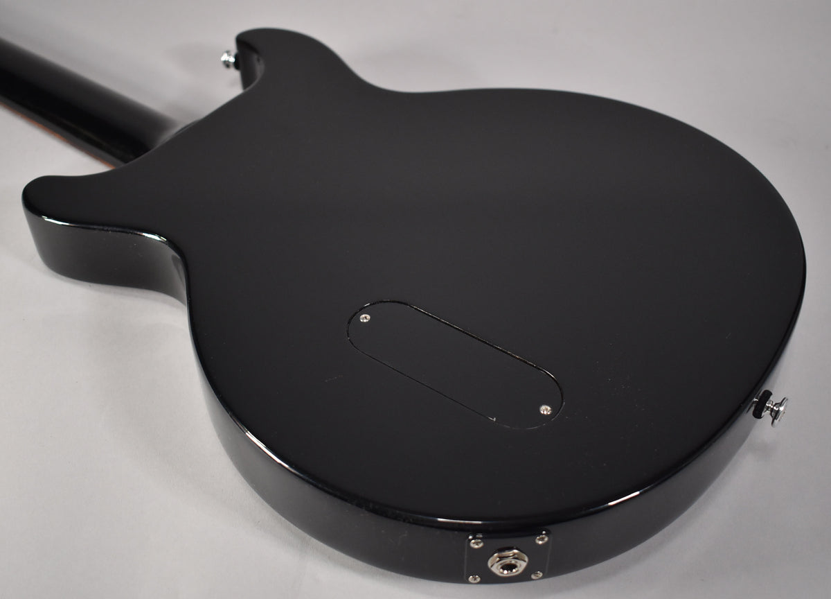 The back of a glossy black guitar body, angled from the neck joint to the output jack, with a control cavity cover.