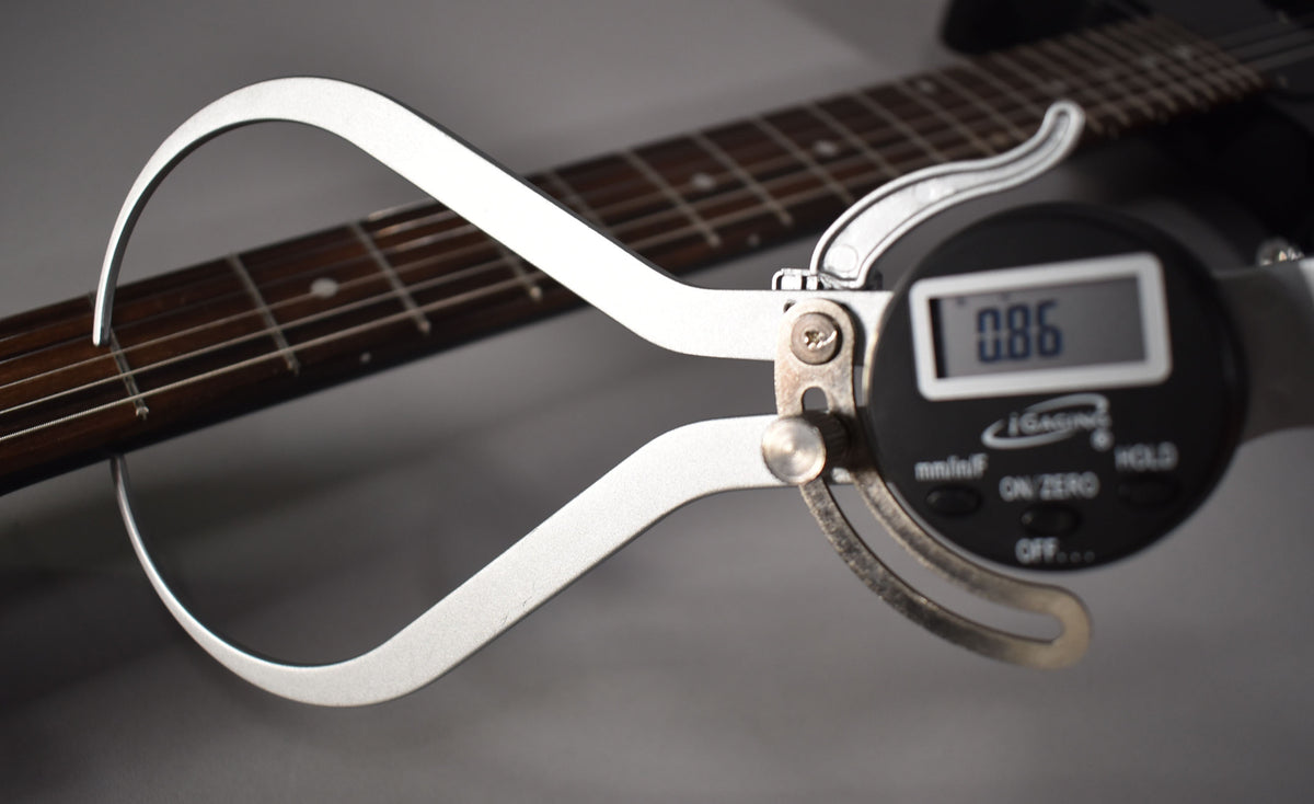 Close-up of a digital fret height gauge measuring the frets on the dark rosewood fretboard of the ebony guitar.