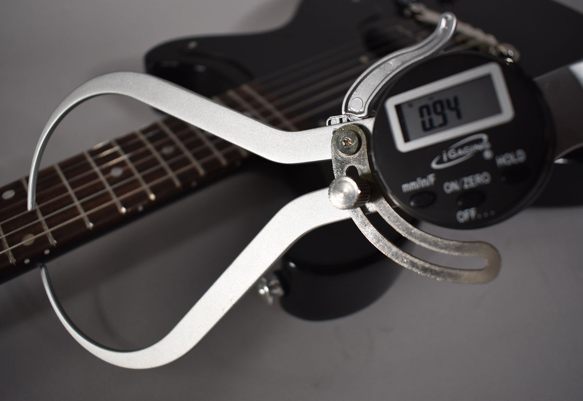 A digital caliper measures the guitar's nut width at 0.94 inches, with the ebony fretboard visible in the background.