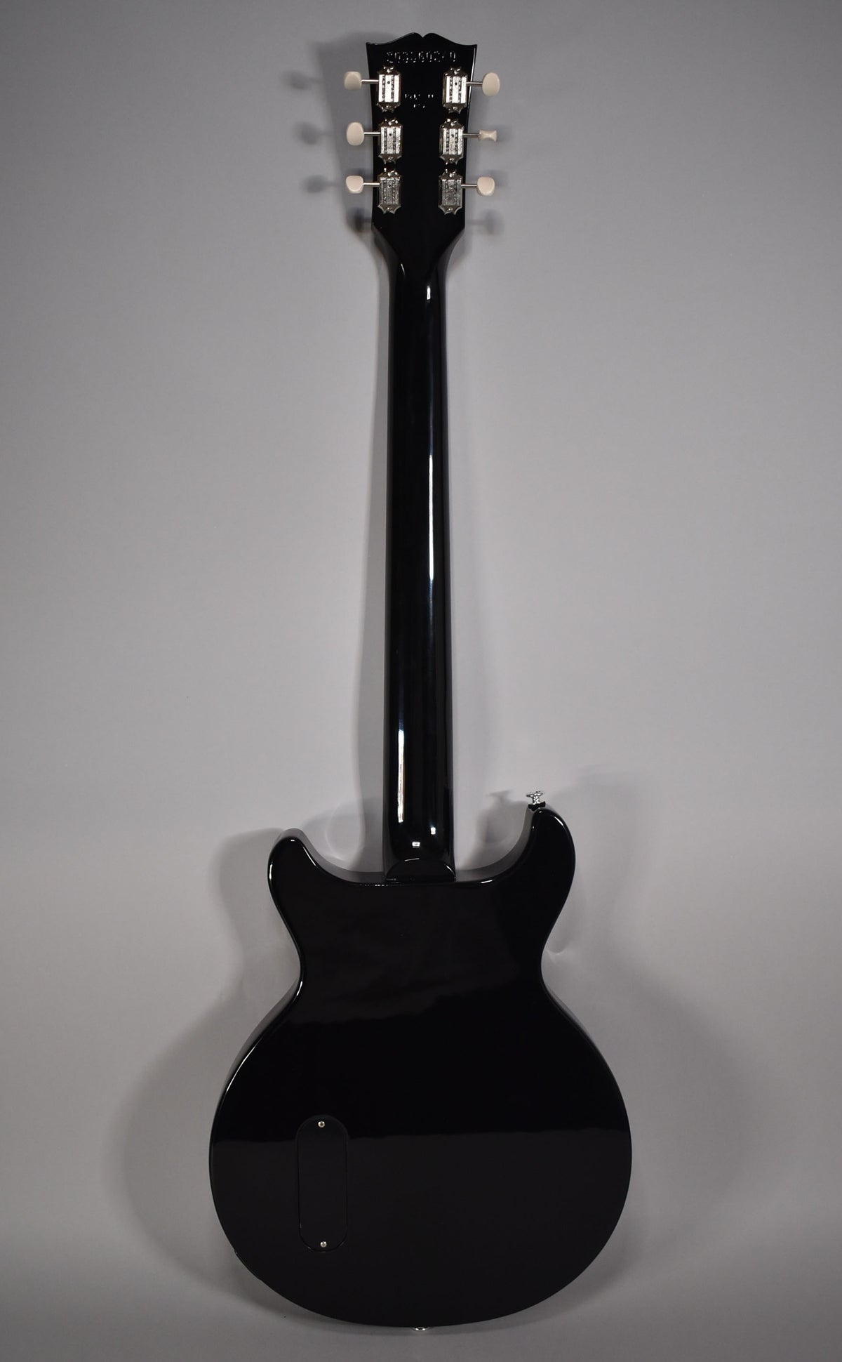 The back of a glossy black electric guitar, with six white-button tuners on the headstock and a control cavity cover on the body.