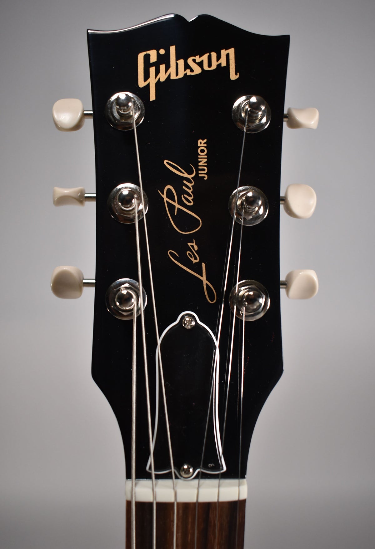 Close-up of a black Gibson Les Paul Junior headstock with cream tuning pegs and gold lettering.