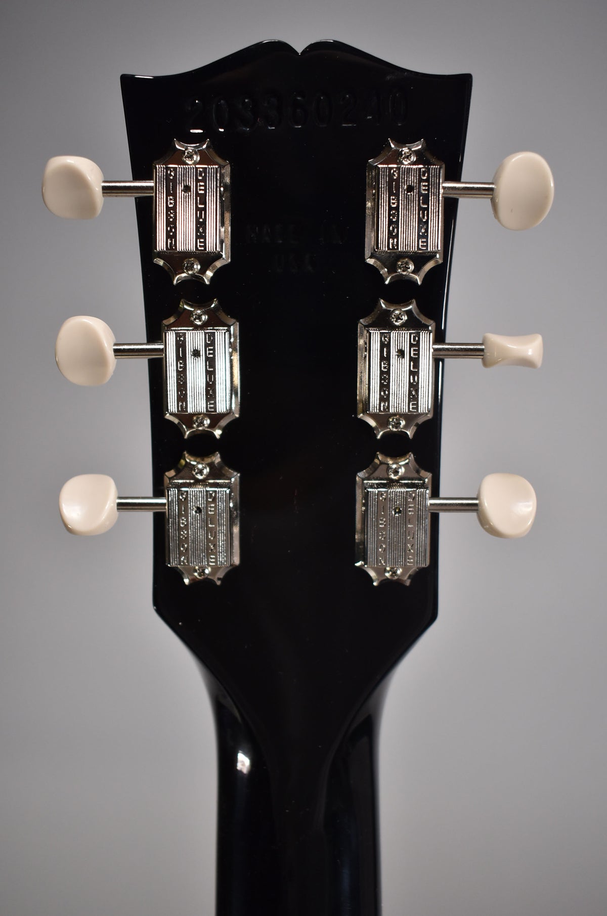Rear view of the guitar's glossy black headstock and neck, showing six chrome tuners with cream buttons.