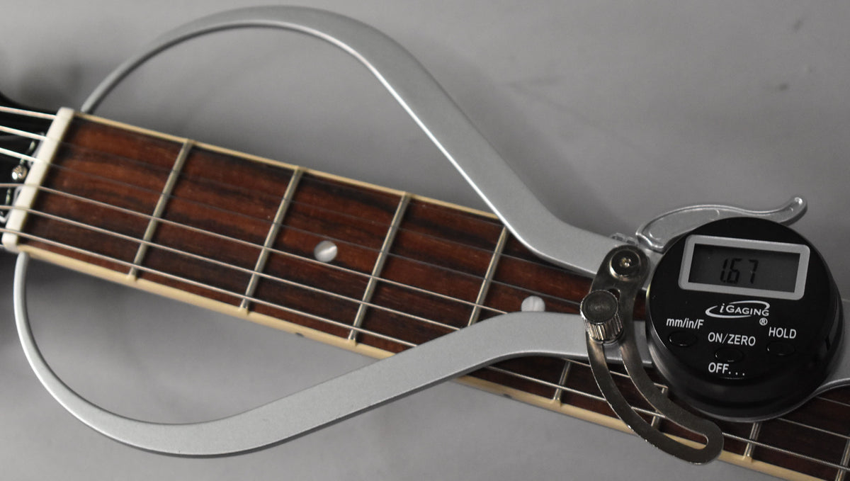 Close-up of the guitar's dark rosewood fretboard with dot inlays, showing a digital caliper measuring the fret height at 1.67mm.